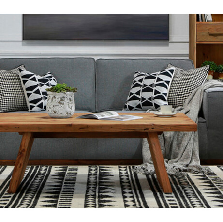 Front view of grey couch with black and white geometric scatter cushions and rug, with a wooden rectangular coffee table